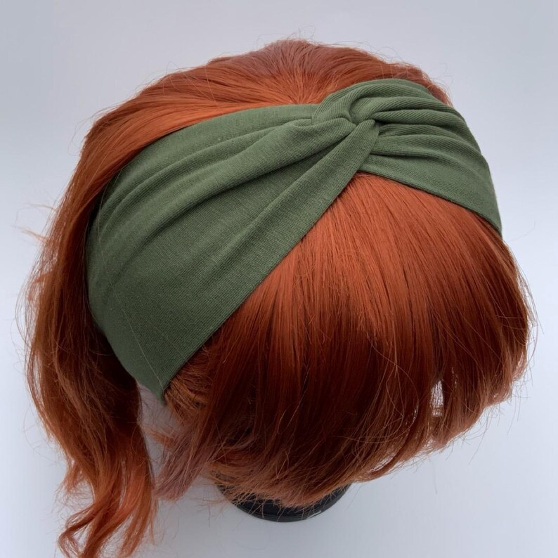 Pu&ograve; includere: Una fascia verde oliva con un design annodato. La fascia &egrave; realizzata in tessuto morbido e viene mostrata su una testa con capelli rossicci. La fascia &egrave; un accessorio elegante per vari acconciature.