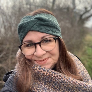 Puede incluir: Una mujer con una diadema verde oscuro y una bufanda de punto marr&oacute;n y beige. Lleva gafas y tiene el pelo casta&ntilde;o.
