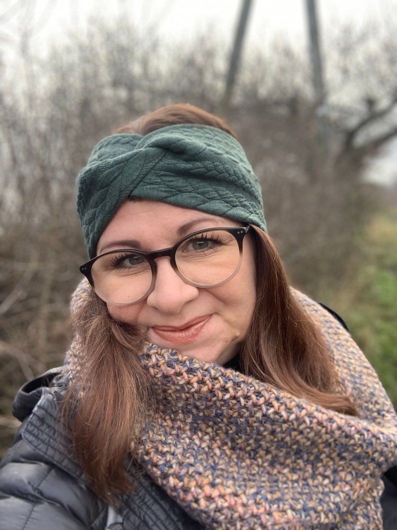 Puede incluir: Una mujer con una diadema verde oscuro y una bufanda de punto marr&oacute;n y beige. Lleva gafas y tiene el pelo casta&ntilde;o.