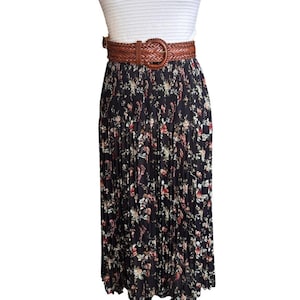 May include: A black pleated skirt with a floral pattern in red, white, and yellow. The skirt is paired with a brown woven belt with a large buckle. A white top is visible above the belt.