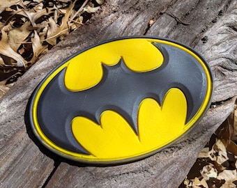 Könnte beinhalten: Ein schwarzer und gelber Batman-Logo-Patch. Das Logo ist im klassischen Stil mit einer gelben Fledermaus-Silhouette auf schwarzem Hintergrund.