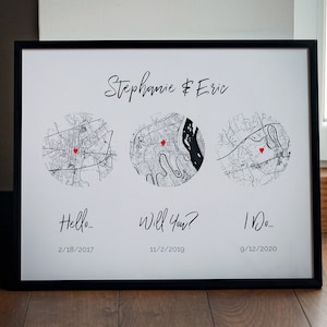 May include: Black and white framed print with three maps of different locations. Each map has a red heart marking a spot. The text "Stephanie & Eric" is at the top of the print. Below each map is a date and a phrase: "Hello - 2/18/2017", "Will You? 11/2/2019", and "I Do - 9/12/2020".