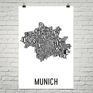 May include: A black and white typography art print of the city of Munich, Germany. The print features the names of the city's districts and neighborhoods arranged in a shape resembling the city's outline. The word "Munich" is printed in large letters at the bottom of the print.