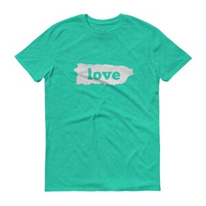 Puede incluir: Una camiseta turquesa con la palabra "love" impresa en letras blancas sobre un rect&aacute;ngulo gris claro texturizado. La camiseta est&aacute; hecha de un material suave y tiene cuello redondo.