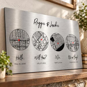 Puede incluir: Una placa de pared de metal plateado cepillado con los nombres Reggie & Jackie en la parte superior. Debajo hay cuatro mapas de calles circulares en blanco y negro, cada uno marcado con un pequeño corazón rojo, acompañados del texto Hello... May 25, 2006, Will You? July 27, 2013, I Do... April 5, 2014 e It's a Boy! August 25, 2016.