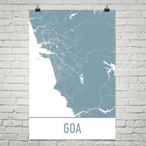 May include: A poster featuring a map of Goa in shades of blue and white, with intricate line details representing roads and waterways. The word "GOA" is printed in a clean, sans-serif font at the bottom of the poster. The poster is hanging on a white brick wall.