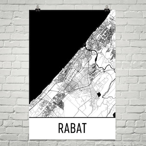 Può includere: Una mappa in bianco e nero di Rabat, Marocco, stampata su un poster. La mappa mostra la disposizione della città con strade ed edifici, a contrasto con uno sfondo nero. La parola "RABAT" è stampata in grassetto nero in basso.