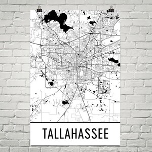 May include: Black and white map print of Tallahassee, Florida. The map shows the city's streets, parks, and bodies of water. The city name is printed in bold, black letters at the bottom of the print.