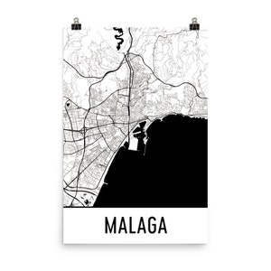 May include: A black and white map of Malaga, Spain, printed on a poster. The map shows the city's layout, including streets, buildings, and the coastline. The word "MALAGA" is printed in a bold, black font at the bottom of the poster.