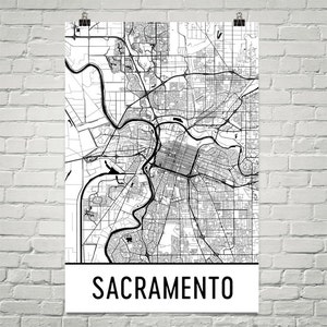 May include: Black and white map of Sacramento, California. The map shows the city's streets, rivers, and other features. The word "Sacramento" is printed in black at the bottom of the map.