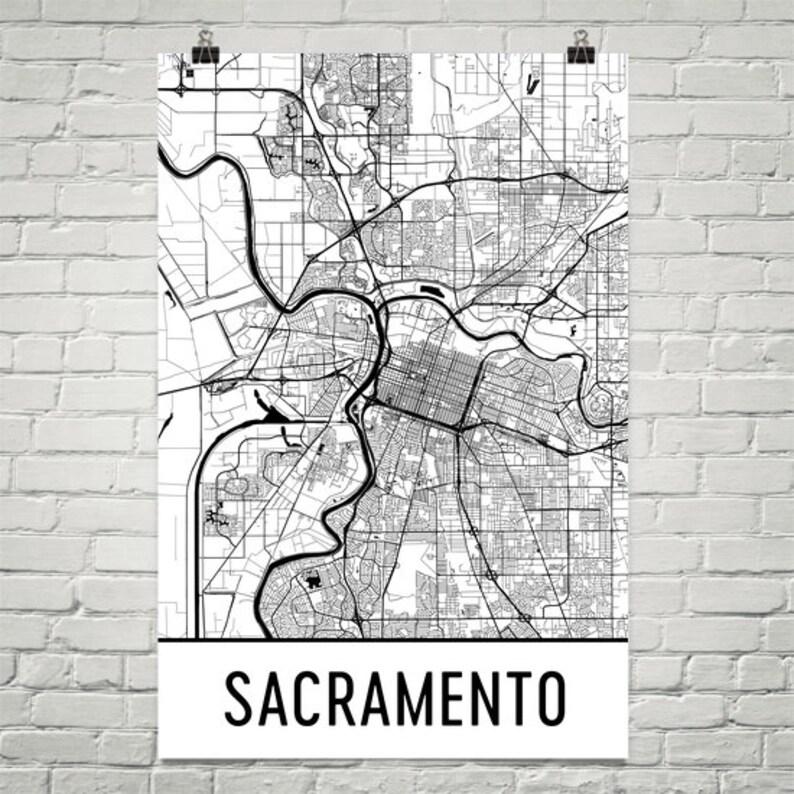 May include: Black and white map of Sacramento, California. The map shows the city's streets, rivers, and other features. The word "Sacramento" is printed in black at the bottom of the map.