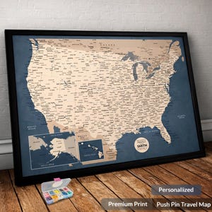 May include: Framed push pin travel map of the United States with a dark blue background and a tan map. The map includes the text "SMITH FAMILY" and the words "Personalized", "Premium Print", and "Push Pin Travel Map". A small container of push pins is in the foreground.