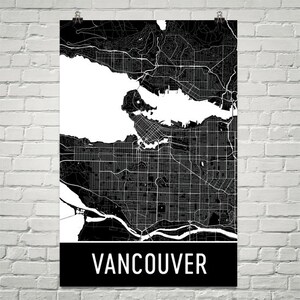 May include: Black and white map of Vancouver, Canada, displayed on a poster. The map shows the city's streets, waterways, and surrounding areas. The word "VANCOUVER" is printed in white on a black banner at the bottom of the poster.