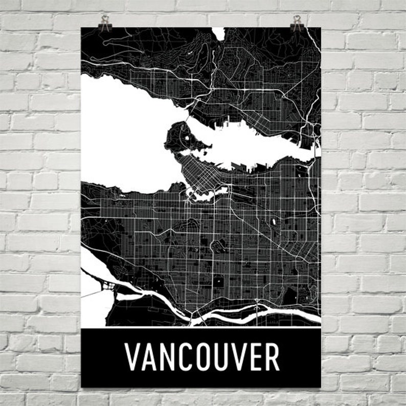 May include: Black and white map of Vancouver, Canada, displayed on a poster. The map shows the city's streets, waterways, and surrounding areas. The word "VANCOUVER" is printed in white on a black banner at the bottom of the poster.