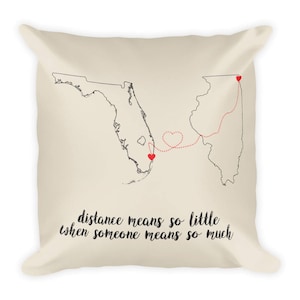 May include: A beige throw pillow with a black and white outline of Florida and Illinois with a red dotted line connecting the two states. The line is shaped like a heart. The text "distance means so little when someone means so much" is printed on the pillow.