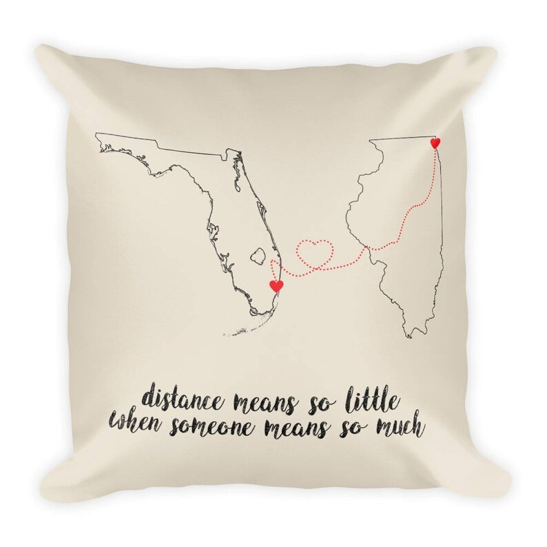 May include: A beige throw pillow with a black and white outline of Florida and Illinois with a red dotted line connecting the two states. The line is shaped like a heart. The text "distance means so little when someone means so much" is printed on the pillow.