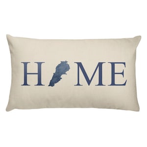 Op de afbeelding: Rechthoekig beige kussen met het woord "HOME" in marineblauw gedrukt. De "O" is vervangen door een marineblauwe kaart van Libanon. Een decoratief kussen voor in huis.