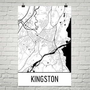May include: A black and white map of Kingston, with roads, rivers, and other geographical features. The word "KINGSTON" is printed in bold, black letters at the bottom of the poster. The poster is hanging on a white brick wall.
