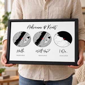 May include: A framed rectangular wall art piece featuring the names Adrienn & Kent in black script. Below are three circular map illustrations with red heart markers, labeled Hello... 09.16.2012, Will You? 09.16.2013, and I Do... 03.01.2014.