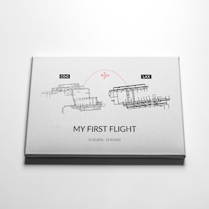May include: A white canvas print with a black and white illustration of two airport layouts, one labeled "CDG" and the other "LAX". A red dotted line with a small airplane icon connects the two layouts. The text "MY FIRST FLIGHT" and "11.20.2022 - 11.30.2022" is printed below the illustration.
