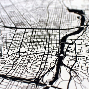 May include: Black and white map of a city with a river running through it. The map shows the streets and roads of the city.