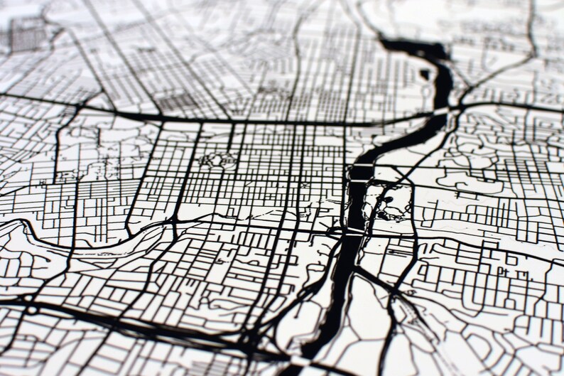 May include: Black and white map of a city with a river running through it. The map shows the streets and roads of the city.