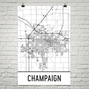 May include: Black and white street map of Champaign, Illinois. The map shows the city's streets, roads, and landmarks. The city name "Champaign" is printed in black at the bottom of the map.