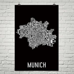 May include: A black and white typography art print of the city of Munich, Germany. The print features the names of the different districts of Munich arranged in the shape of the city's outline. The text "MUNICH" is printed in white at the bottom of the print.