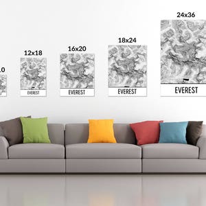 May include: A living room interior with a gray couch and five framed prints of a black and white topographic map of Mount Everest. The prints are in various sizes, including 8x10 inches, 12x18 inches, 16x20 inches, 18x24 inches, and 24x36 inches. Each print has the word "EVEREST" printed below the map.