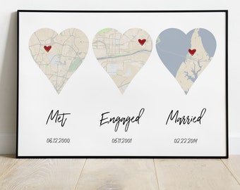 May include: A framed print featuring three heart-shaped map designs, each with a red heart marking a location. The words "Met," "Engaged," and "Married" are written below the hearts, along with dates.