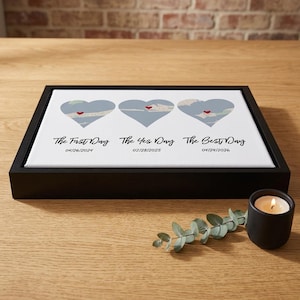 Puede incluir: Impresión en lienzo enmarcada con tres diseños de mapas en forma de corazón azul, cada uno con un corazón rojo. Debajo de los corazones están las frases "The First Day", "The Yes Day" y "The Best Day" con fechas. Una vela encendida y vegetación en primer plano.