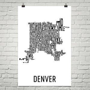May include: A white poster with a black map of Denver, Colorado, composed of neighborhood names. The word "DENVER" is printed in a bold, sans-serif font at the bottom of the poster. The poster is hanging on a white brick wall.