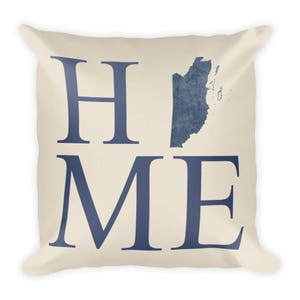 Puede incluir: Una almohada beige con la palabra "HOME" en letras azules. La "O" de "HOME" se reemplaza con un contorno azul del país de Belice.