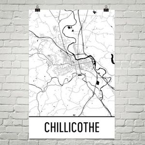 May include: A black and white map of Chillicothe, Ohio, with roads, rivers, and buildings. The city name is printed in bold, black letters at the bottom of the poster. The map is printed on white paper and is held by two silver clips.