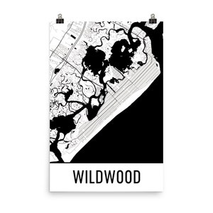 May include: A black and white map print of Wildwood, New Jersey. The map shows the coastline, waterways, and streets. The word "WILDWOOD" is printed in a bold, sans-serif font at the bottom of the print. The print is held by two silver binder clips.