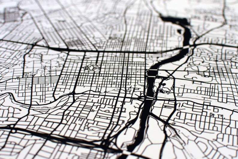 May include: Black and white detailed map print. The map features a network of roads, streets, and a river, creating a complex urban landscape. The design is a close-up view, highlighting the intricate details of the city's layout.