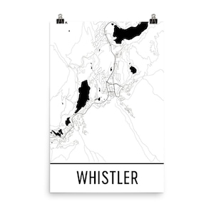 May include: A black and white map print of Whistler, featuring the town's layout with roads, lakes, and surrounding terrain. The word "WHISTLER" is printed in a bold, sans-serif font at the bottom of the print. The print is held by two silver binder clips.