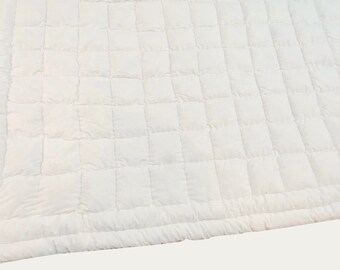 Könnte beinhalten: Eine einfarbige weiße Steppdecke mit einem gleichmäßigen Gittermuster aus quadratisch abgesteppten Abschnitten. Der Stoff weist eine weiche, leicht bauschige Textur auf der gesamten Oberfläche auf und erzeugt ein konsistentes Steppmuster.