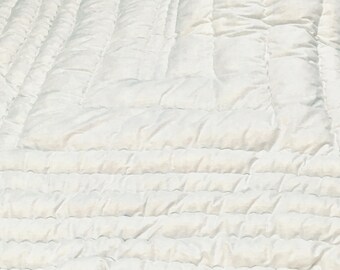 Könnte beinhalten: Eine einfarbige, weiße Steppdecke mit einem sich wiederholenden rechteckigen Steppmuster. Der Stoff hat eine weiche, bauschige Textur, die durch das Gitter aus parallelen Linien entsteht, welche konzentrische Ränder über die gesamte Fläche bilden.