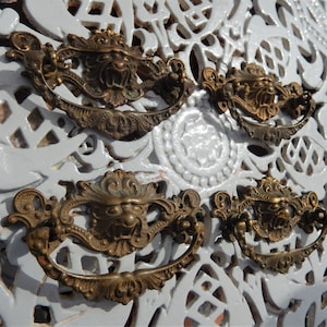 May include: Four antique brass cabinet pulls with ornate designs featuring a lion's head. The pulls have a loop handle and are in good condition.