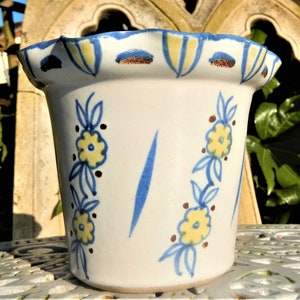 May include: A white ceramic flower pot with a blue and yellow floral design. The pot has a scalloped rim and is decorated with brown dots.