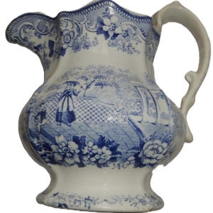 May include: A white ceramic jug featuring a blue transferware pattern. The design includes floral borders, architectural columns, and a figure standing on a terrace. It has a curved handle, a scalloped rim, and a wide pouring spout.