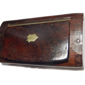 May include: A small, rectangular wooden box with a hinged lid. The box is made of dark brown wood and features a brass accent in the shape of a stylized flower. The box has a simple, classic design.