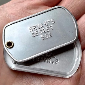 K&ouml;nnte beinhalten: Ein silberner Metall-Hundeanh&auml;nger mit dem Text "Bryan's Secret Box" auf der Vorderseite. Der Anh&auml;nger ist ge&ouml;ffnet und zeigt ein kleineres, silbernes Metallfach.