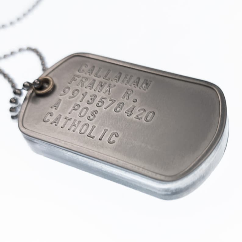 K&ouml;nnte beinhalten: Ein silberner milit&auml;rischer Hundemarkenanh&auml;nger mit dem eingravierten Text "CALLAHAN FRANK R. 9913578420 A POS CATHOLIC".