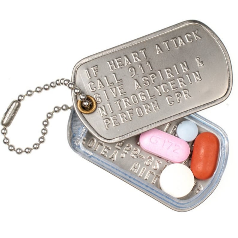 K&ouml;nnte beinhalten: Ein silberner Hundemarkenanh&auml;nger mit einer Kette, die Marke hat den Text "IF HEART ATTACK CALL 911 GIVE ASPIRIN & NITROGLYCERIN PERFORM CPR". Die Marke ist ge&ouml;ffnet, um ein Fach mit mehreren Pillen zu enth&uuml;llen.
