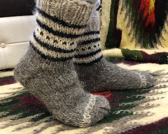 May include: A pair of gray wool socks with black and white stripes. The socks are knitted and have a fuzzy texture.