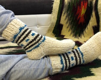Könnte beinhalten: Ein Paar weiße Wollsocken mit blauen und braunen Streifen. Die Socken sind mit einem traditionellen Muster gestrickt und werden an den Füßen getragen.