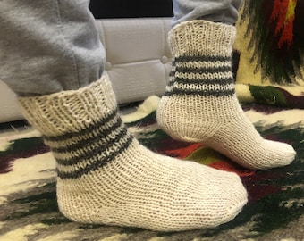 Könnte beinhalten: Ein Paar weiße Stricksocken mit schwarzen Streifen. Die Socken sind aus Wolle und haben eine bequeme Passform.
