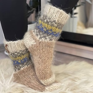 Könnte beinhalten: Ein Paar braune, flauschige Stricksocken mit einem geometrischen Muster in Blau, Gelb und Grau. Die Socken werden an den Füßen einer Person getragen.